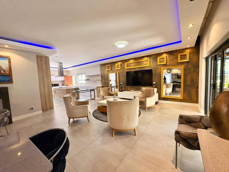 Spacious open-plan living area featuring modern tiled floors, recessed ceiling lighting with blue LED accents, and a contemporary kitchen with a central island.