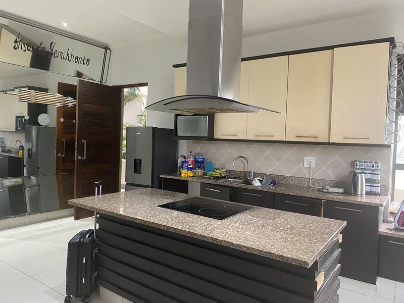 Modern kitchen featuring a central island with an integrated electric hob, stainless steel extractor fan, stone countertops, and ample built-in cabinetry.