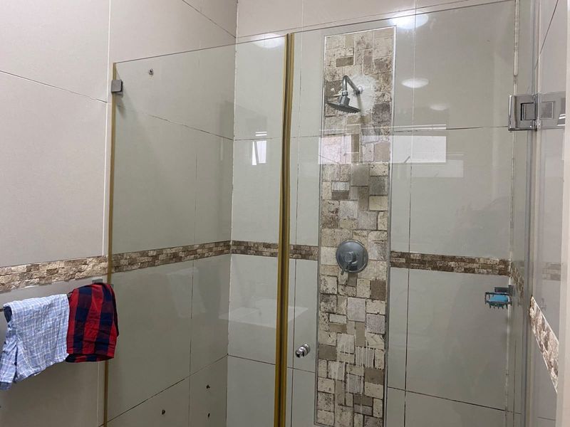 A bathroom shower area featuring a glass enclosure, wall-mounted shower head, and decorative mosaic tile accent strip.