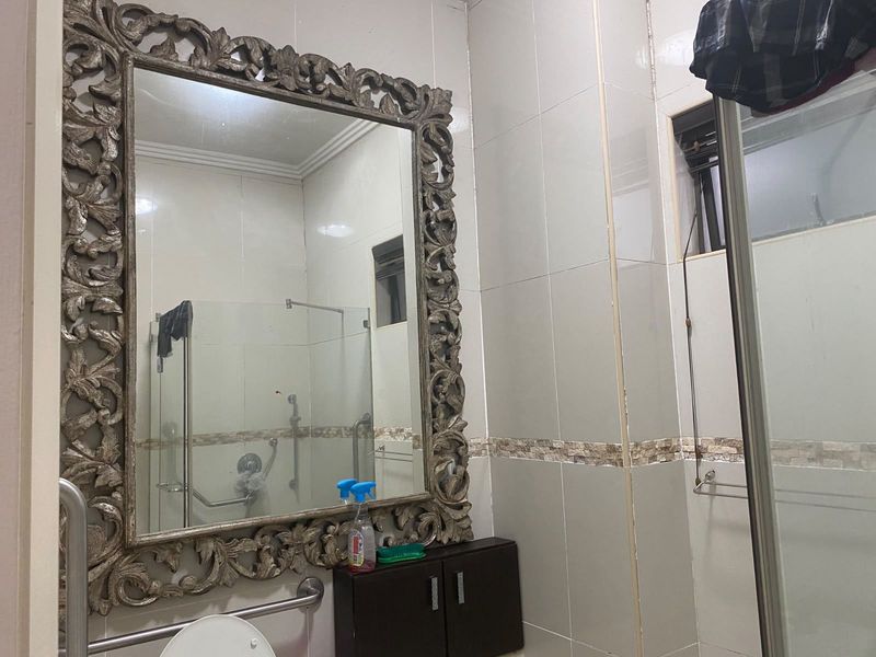 A functional bathroom featuring wall-to-wall tiling, a glass shower enclosure, safety grab rails, and a built-in vanity cabinet with a decorative mirror.