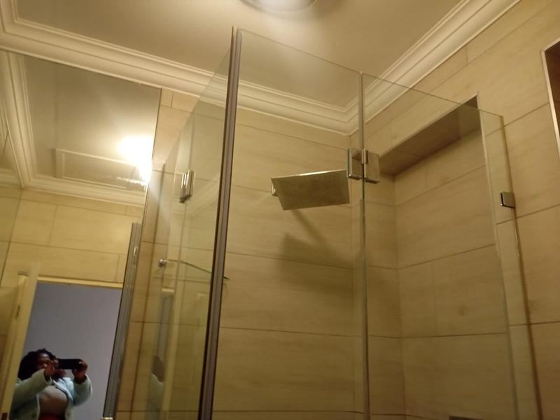 A modern bathroom shower area featuring a glass enclosure, rain shower head, and built-in recessed wall niche with neutral wall tiling.