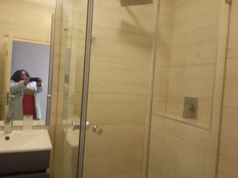 A modern bathroom featuring a glass-enclosed shower, wall-mounted mixer, and a vanity basin with storage cabinet.