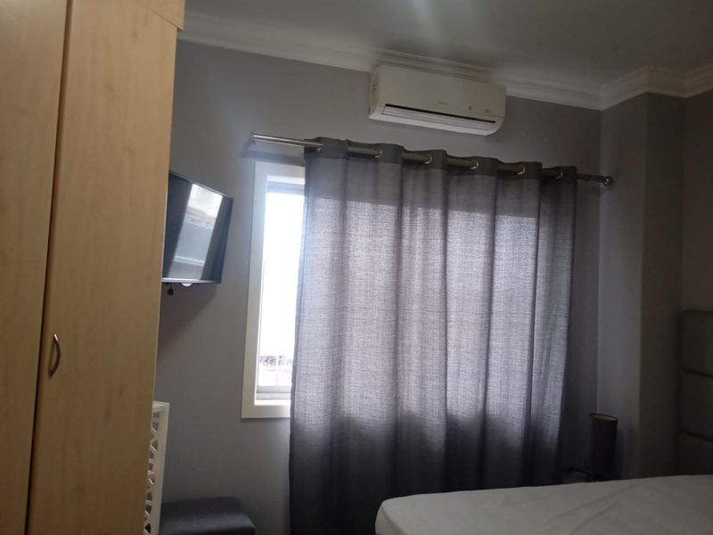A bedroom featuring a wall-mounted split-system air conditioner and a window with a curtain rod.