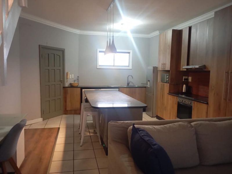 Open plan kitchen and living area featuring wood-finish cabinetry, a central island with breakfast bar, and tiled flooring throughout.