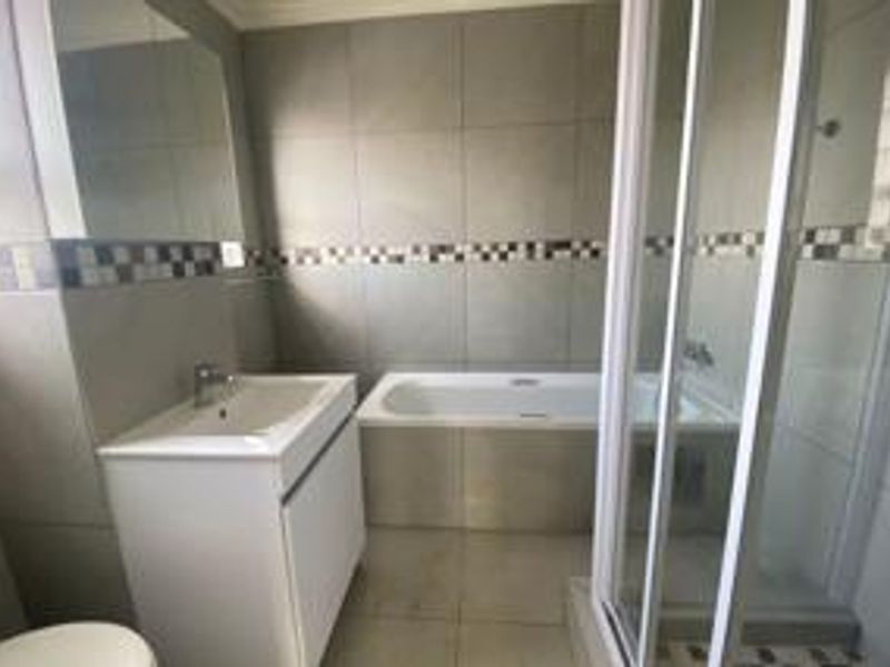A clean, modern bathroom featuring a built-in vanity, a bathtub, and a separate shower enclosure with neutral wall and floor tiling.