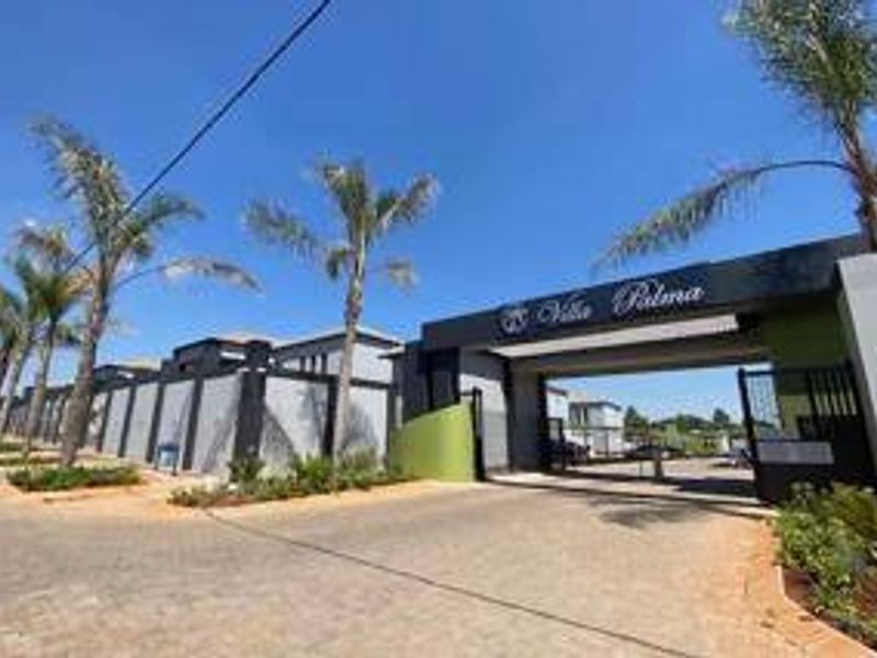 The entrance to Villa Palma featuring a modern gated security access point, perimeter walling, and well-maintained landscaped palm trees along the paved driveway.