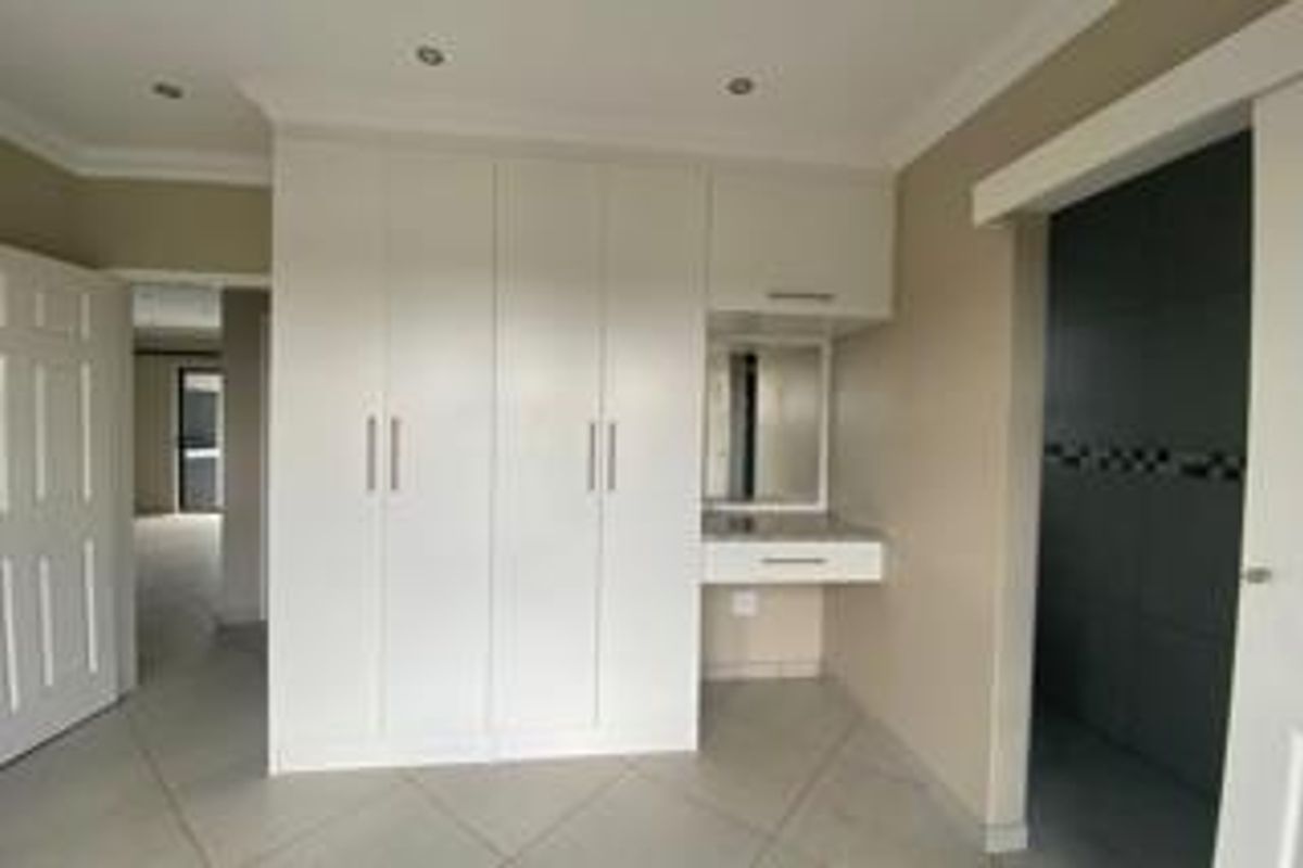 A clean, modern bedroom featuring ample built-in cupboard space, a dedicated vanity area, and neutral tiled flooring with recessed lighting.