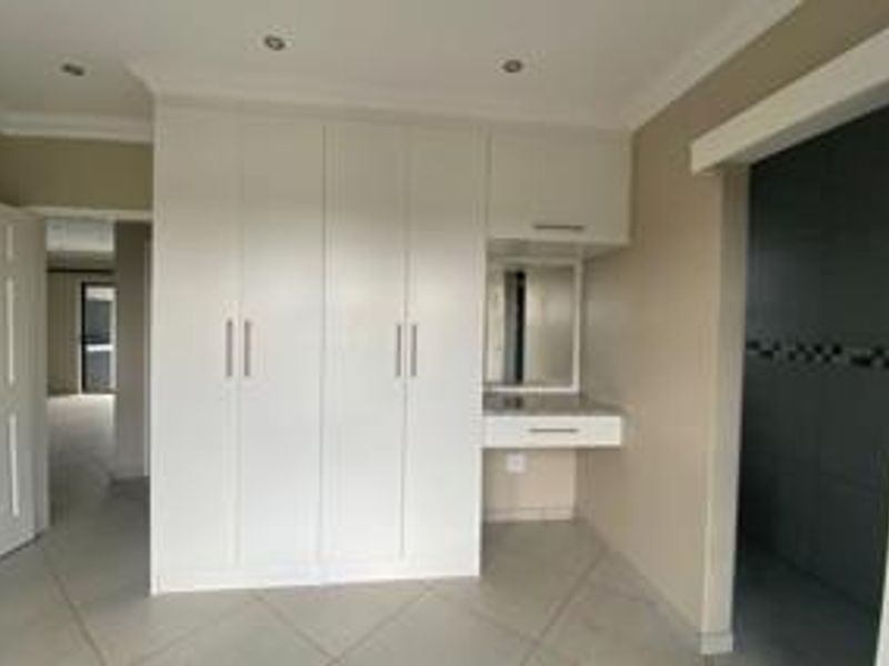 A clean, modern bedroom featuring ample built-in cupboard space, a dedicated vanity area, and neutral tiled flooring with recessed lighting.