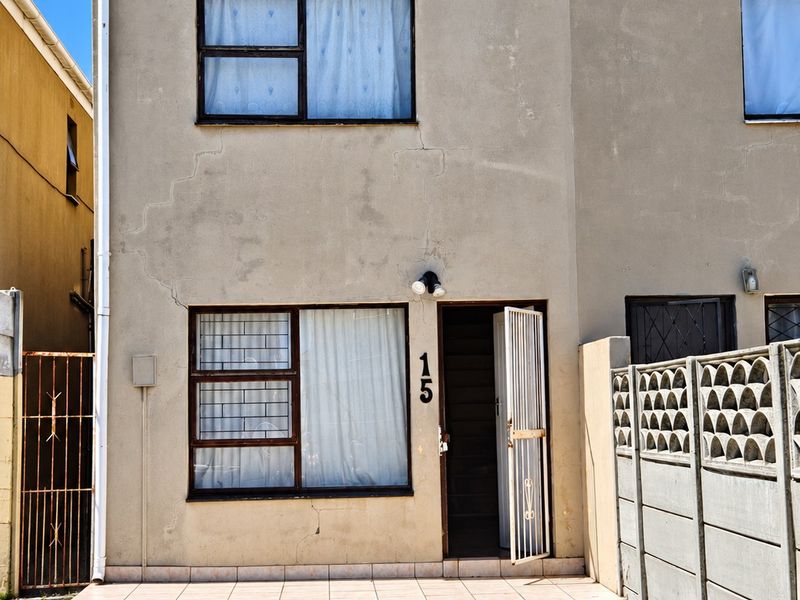Front elevation of a two-story townhouse featuring a tiled entrance porch, security gates, and a concrete driveway with visible exterior maintenance requirements.