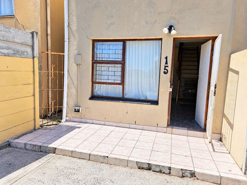 Front entrance of the townhouse featuring a tiled patio area, security gate, and visible exterior wall cracking requiring maintenance.