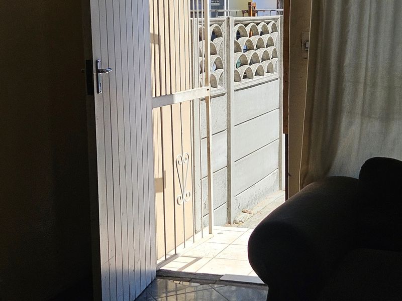 An interior view of an entrance featuring tiled flooring, a white security gate, and a view towards the exterior boundary wall.