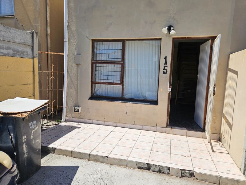 Front entrance of a townhouse featuring a small tiled patio, security gate, and window security bars, showing signs of exterior wear and maintenance needs.