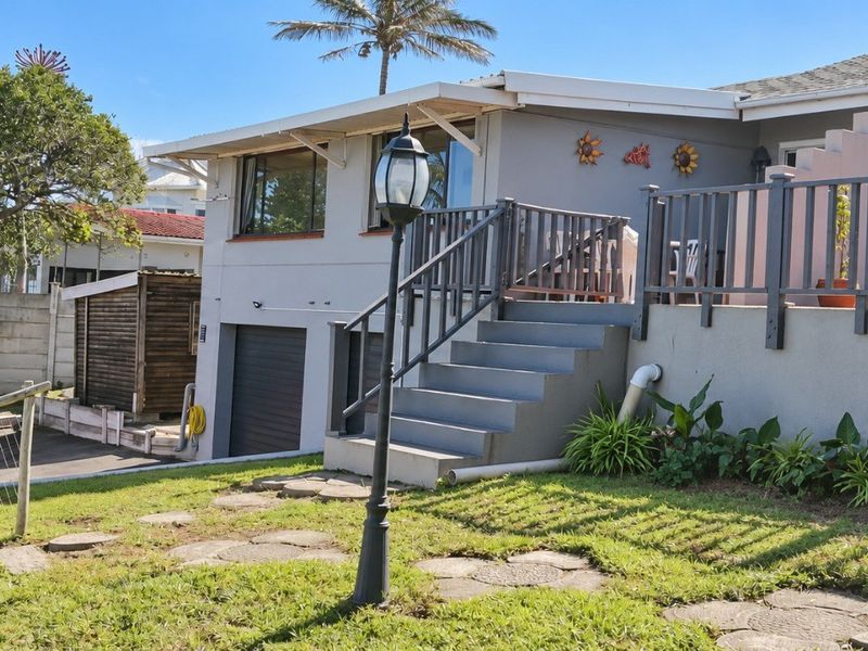 Rear exterior view of the house featuring a raised patio, staircase, garden area, and integrated garage access.