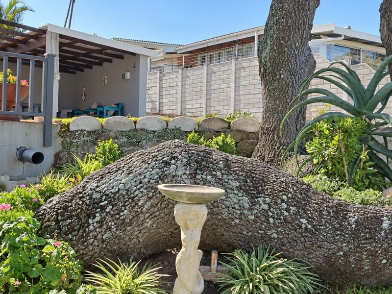 A landscaped garden area featuring mature trees, a stone bird bath, and a raised patio area with a timber pergola structure.