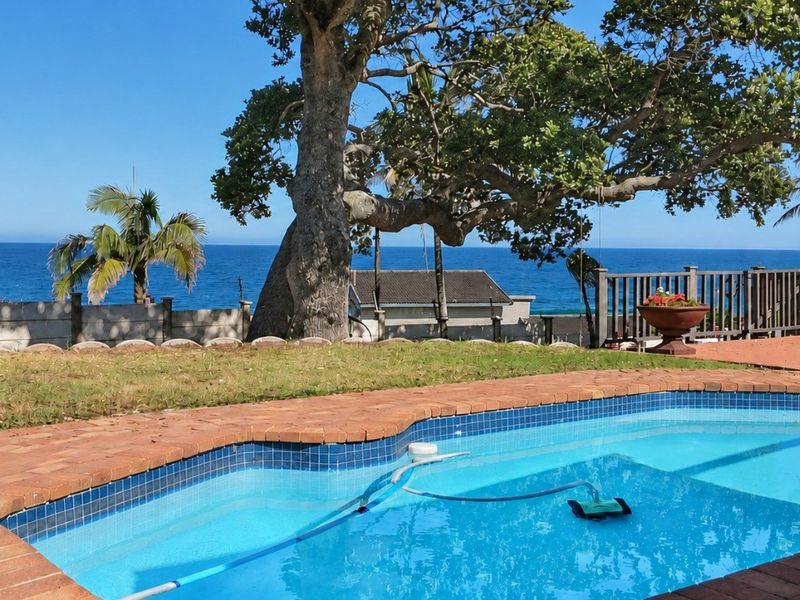 Outdoor pool area featuring a swimming pool with brick coping, paved surround, and ocean views, set against a backdrop of mature trees.