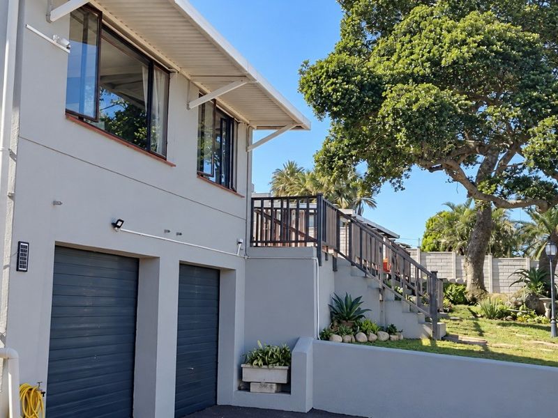 Rear exterior view featuring a double garage, an elevated staircase leading to the upper level, and a landscaped garden area with mature trees.