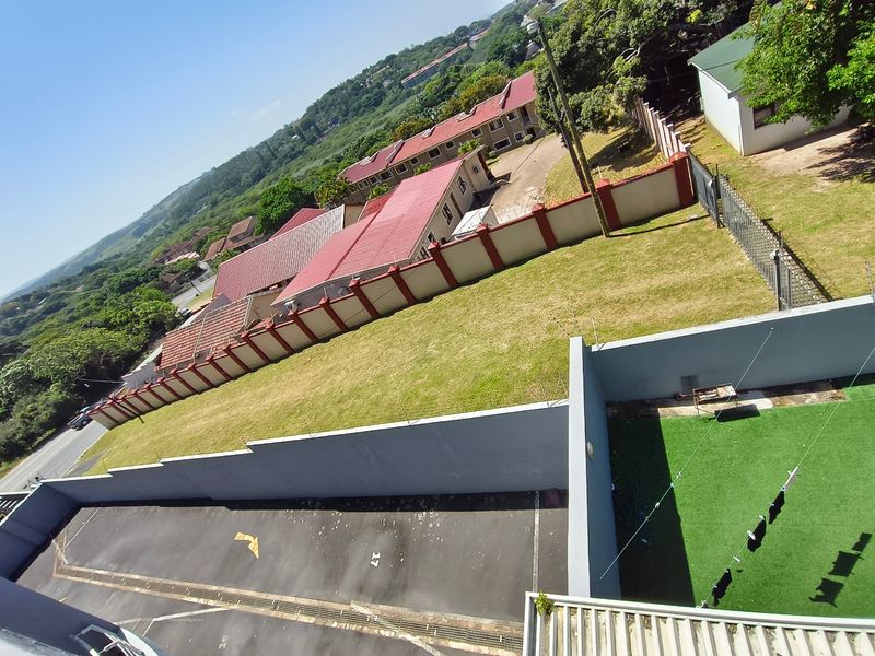 An elevated aerial view of the property grounds, featuring a paved parking area, artificial lawn, and secure perimeter wall with electric fencing.