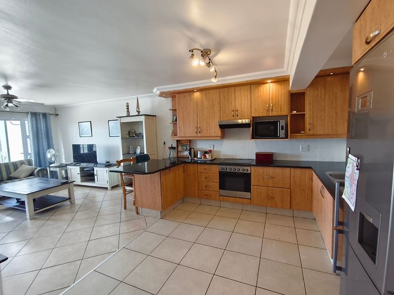 Spacious open-plan living area featuring a well-appointed kitchen with wooden cabinetry, granite countertops, and integrated appliances, flowing into a comfortable lounge space.