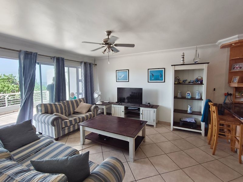 Spacious open-plan living area featuring tiled flooring, a ceiling fan, and large sliding glass doors leading to an outdoor balcony.