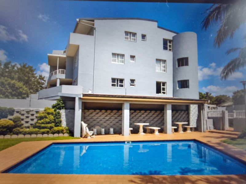 Exterior view of an apartment complex featuring a swimming pool and a covered patio area with paved decking.