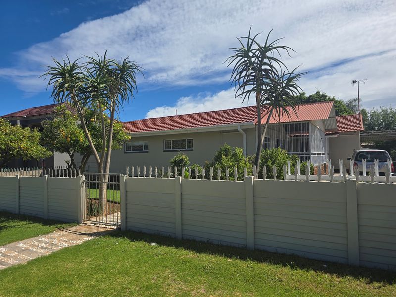Front view of a residential property featuring a secure precast boundary wall with metal spikes, a tiled roof, and established garden landscaping.
