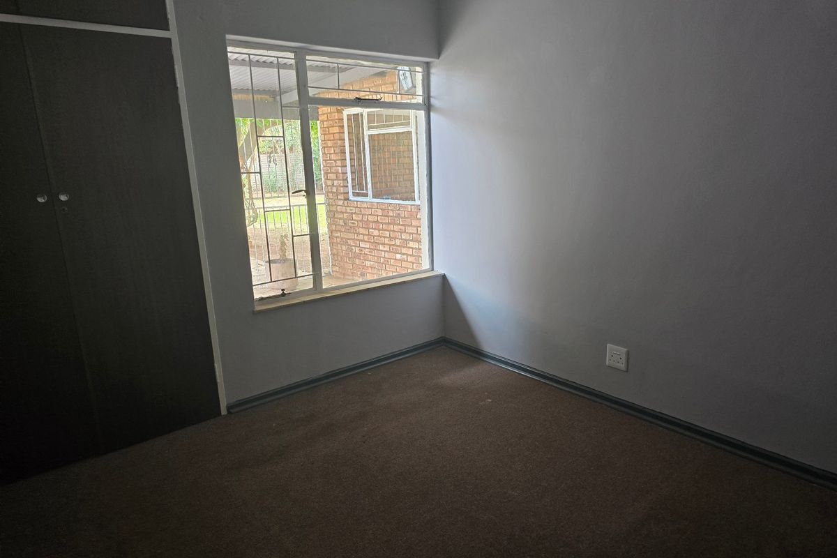 An empty bedroom featuring built-in cupboards, carpeted flooring, and a window with security bars.