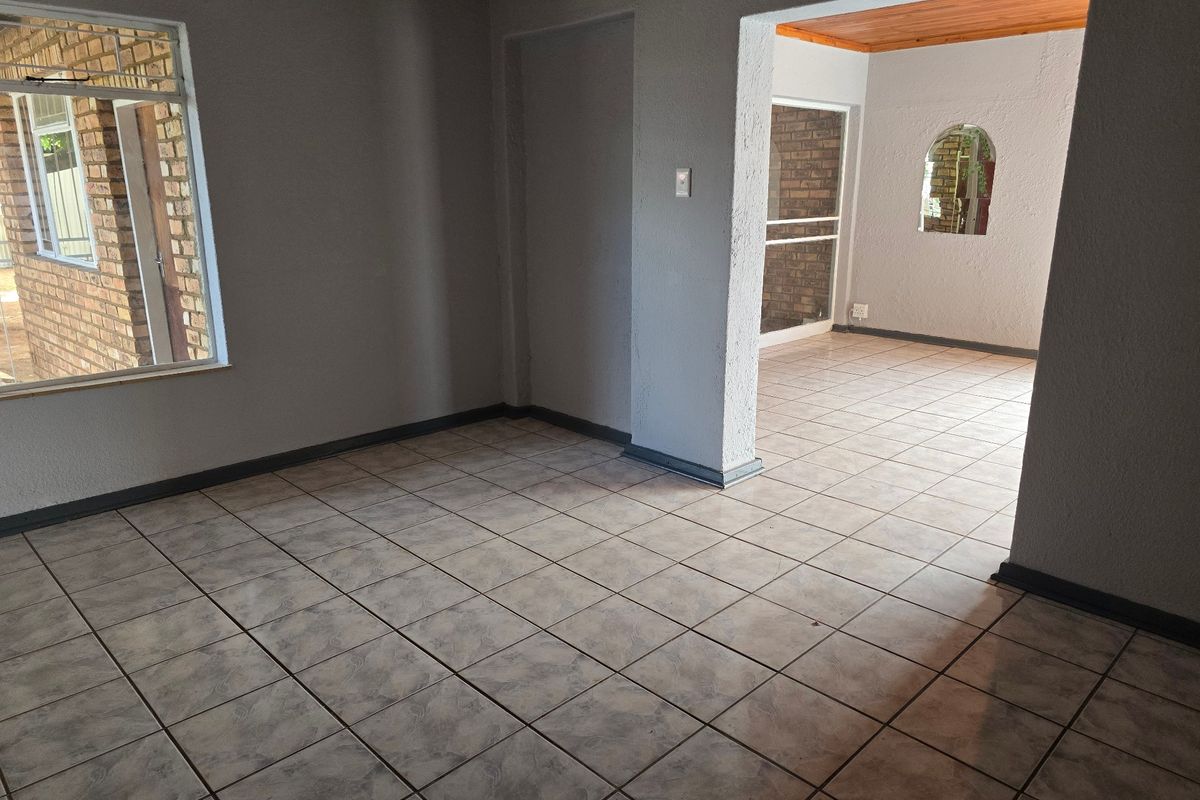 An empty living area featuring ceramic floor tiles, timber ceiling accents, and an open-plan layout connecting to an adjacent space.