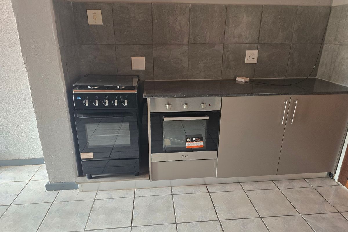 A functional kitchen area featuring a built-in oven, freestanding stove, stone countertops, and tiled backsplash with neutral cabinetry.