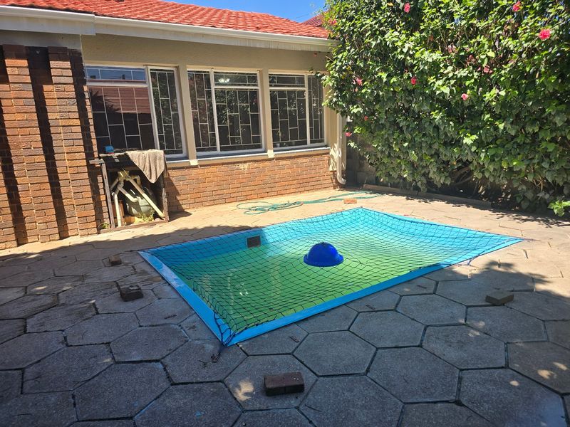 Outdoor pool area featuring a paved patio, brick exterior wall, and a safety net covering the swimming pool.