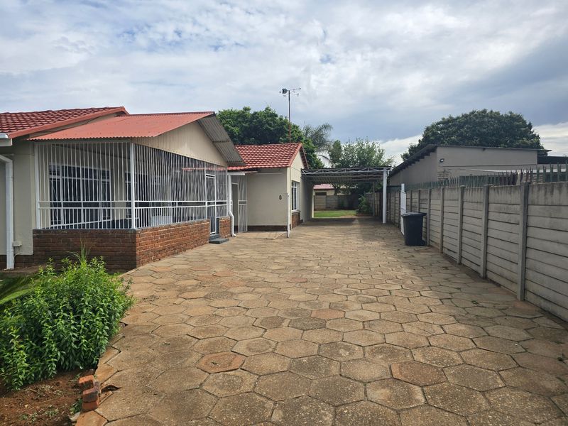Front exterior view of the property featuring a paved driveway, carport, and secure perimeter walling.