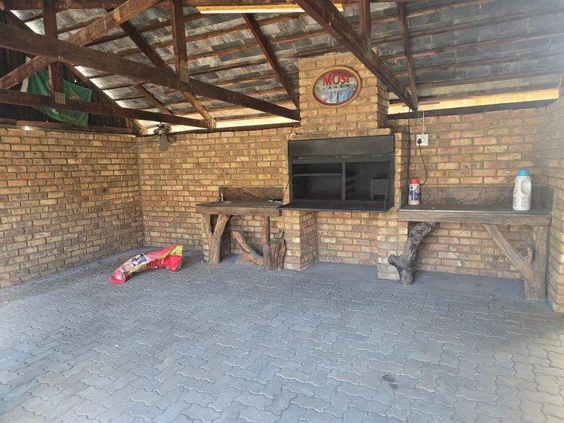 Covered outdoor patio area featuring a built-in braai, rustic stone-look counters, exposed timber roof trusses, and durable paved flooring.