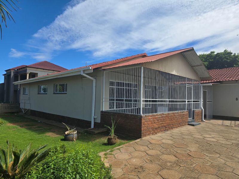 Front exterior view of a single-story house featuring a tiled roof, brick base, and a covered patio area with security bars.