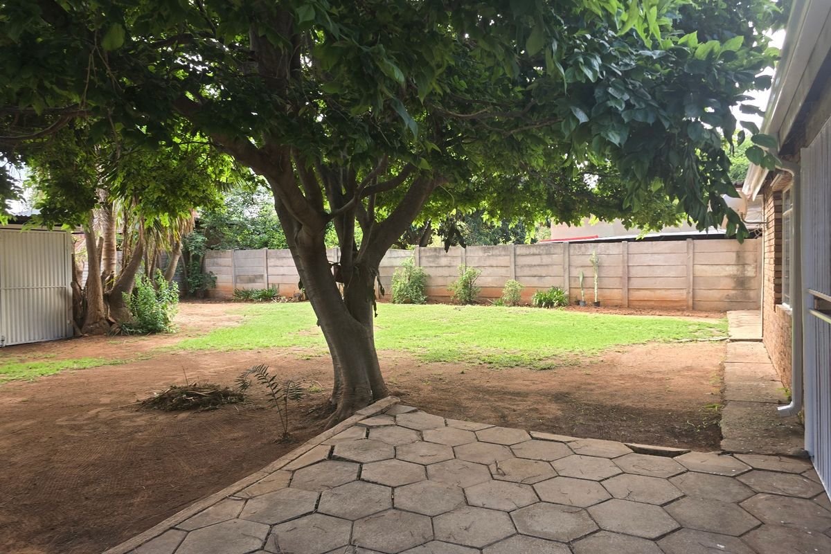 A spacious rear garden featuring a paved patio area, mature tree, and precast concrete boundary walling, offering potential for landscaping and outdoor improvement.