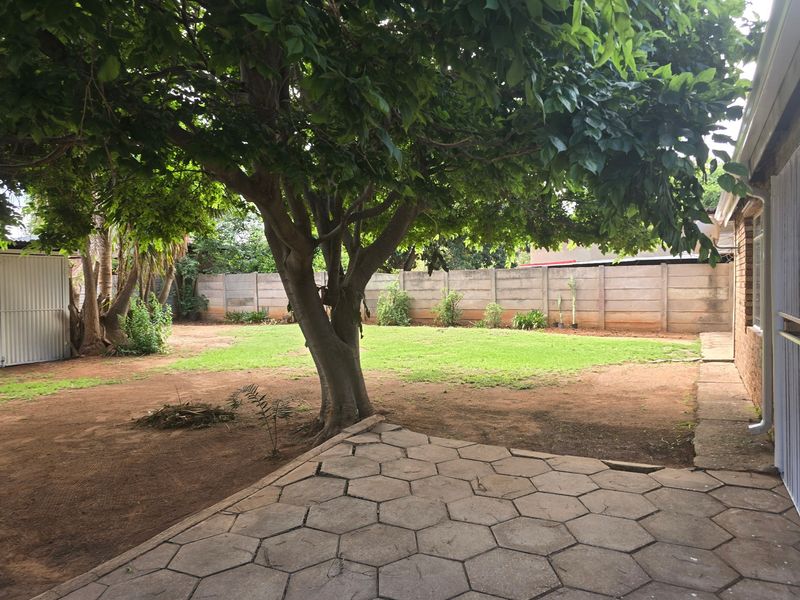A spacious rear garden featuring a paved patio area, mature tree, and precast concrete boundary walling, offering potential for landscaping and outdoor improvement.