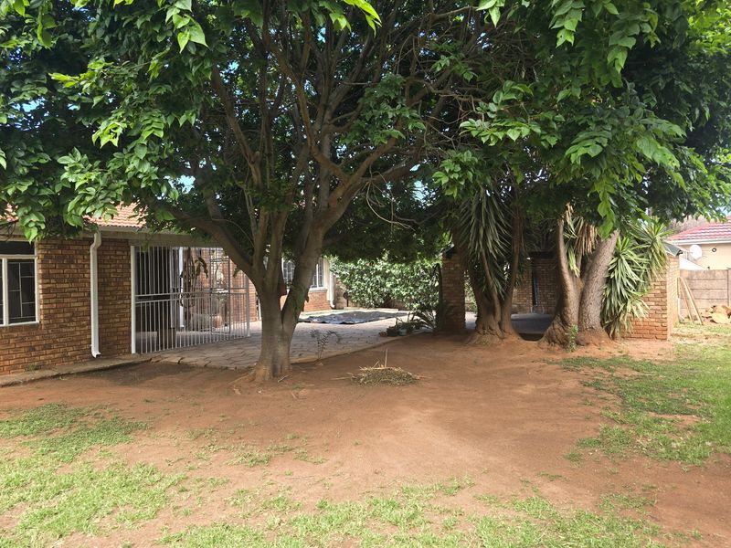 Rear exterior view of the property featuring a brick facade, paved patio area, and mature trees in the garden.