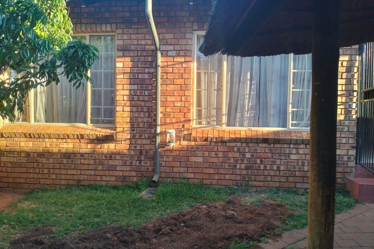 Rear exterior view of the townhouse featuring a face brick facade, downpipe, and a partial view of a thatched lapa structure.