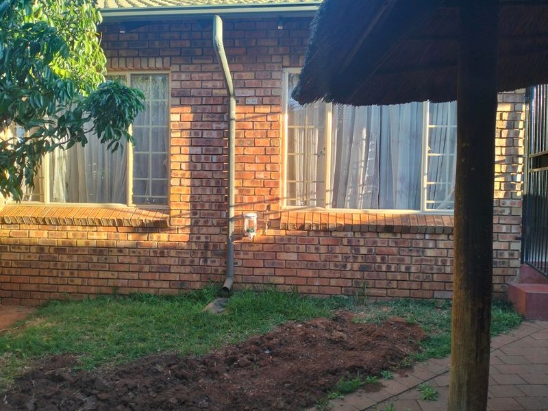 Rear exterior view of the townhouse featuring a face brick facade, downpipe, and a partial view of a thatched lapa structure.