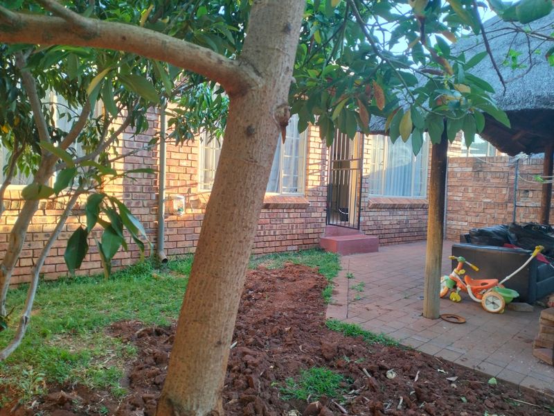 A rear exterior view of the townhouse featuring a face brick facade, a paved patio area, and a thatched roof structure.