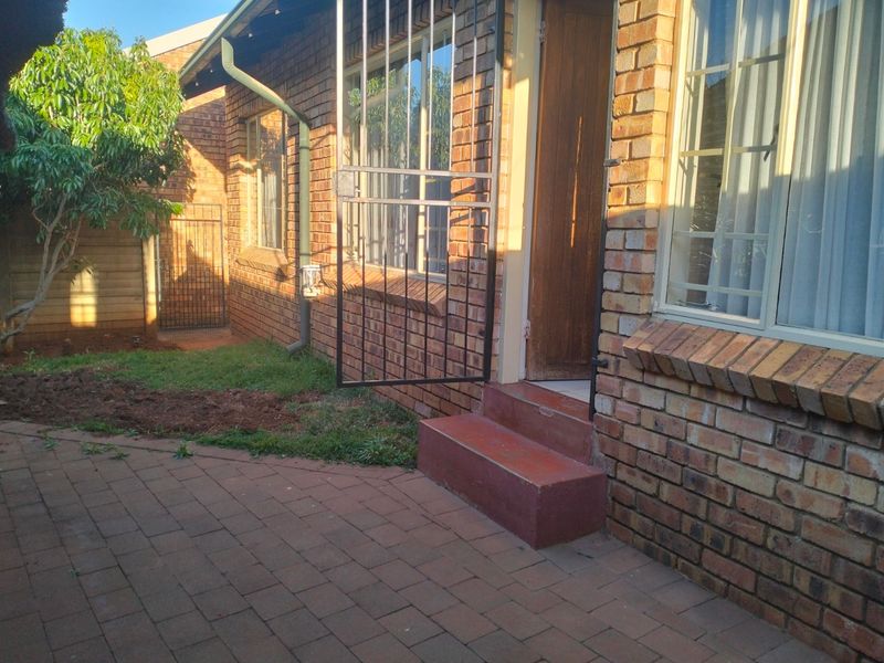 Rear exterior view of the townhouse featuring a paved patio area, brick facade, and security gate access.
