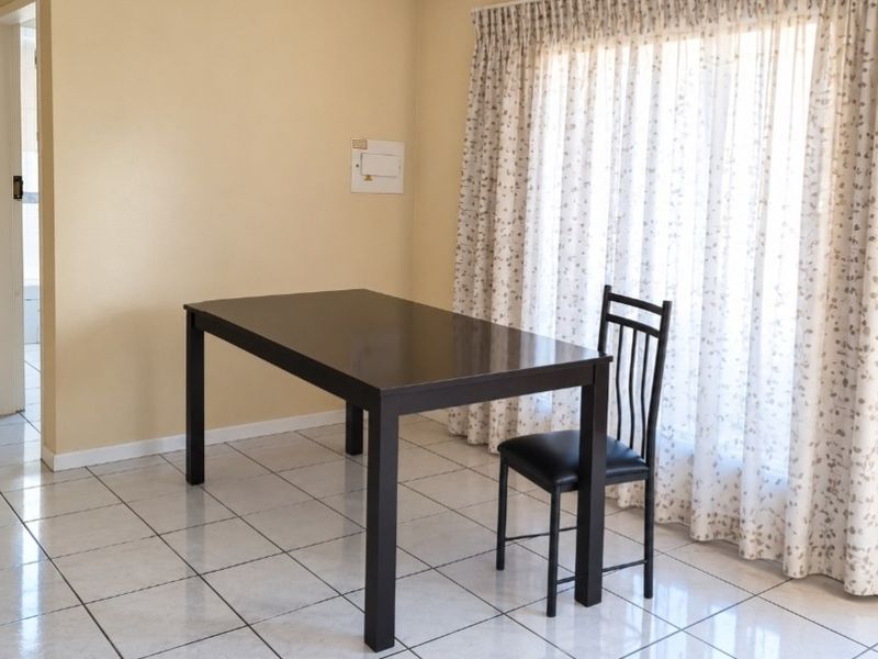 A simple dining area featuring neutral wall paint and light-colored ceramic floor tiles, providing a functional space for meals.