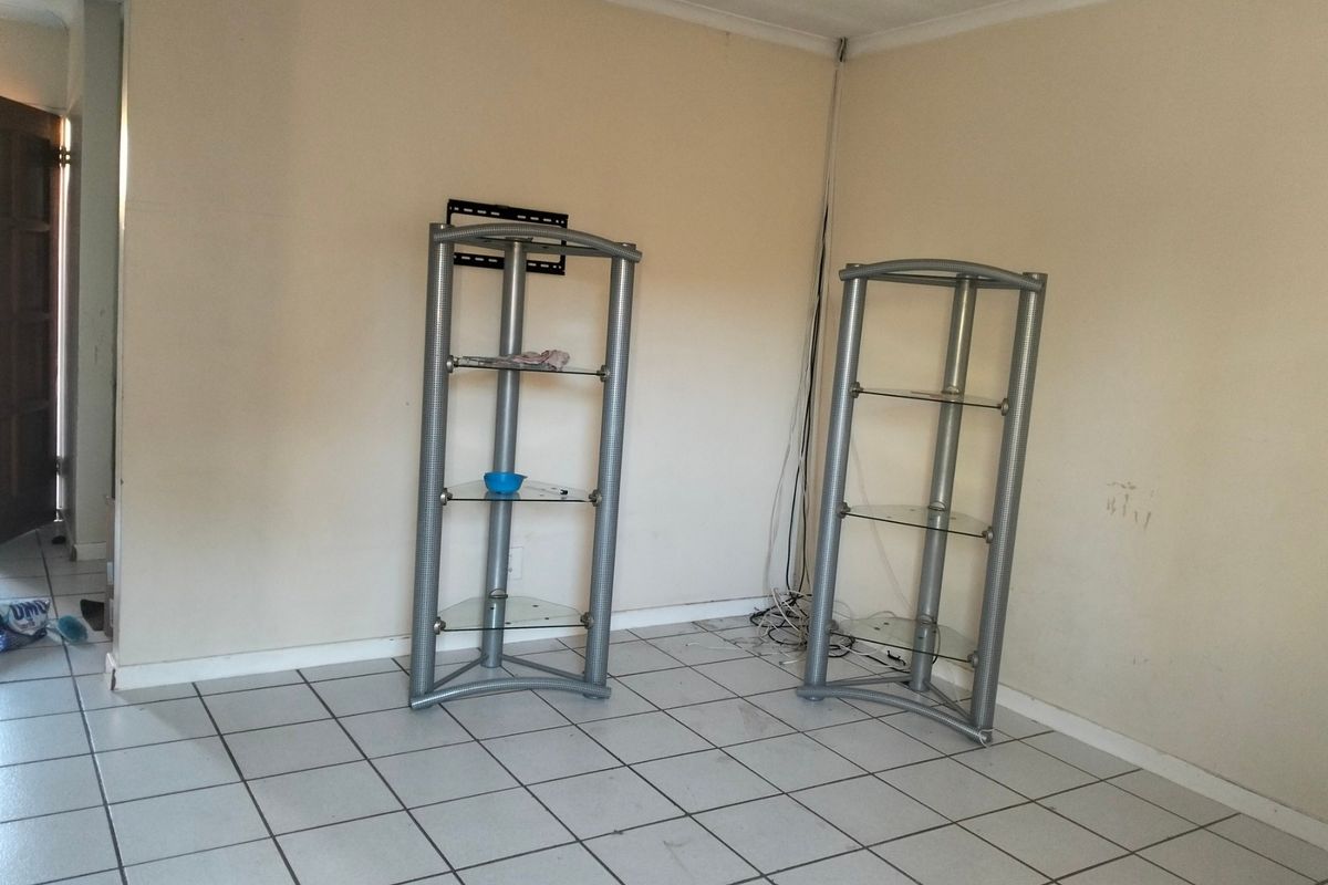 An empty living room area featuring tiled flooring and a wall-mounted television bracket, requiring minor cosmetic updates to the walls and wiring management.