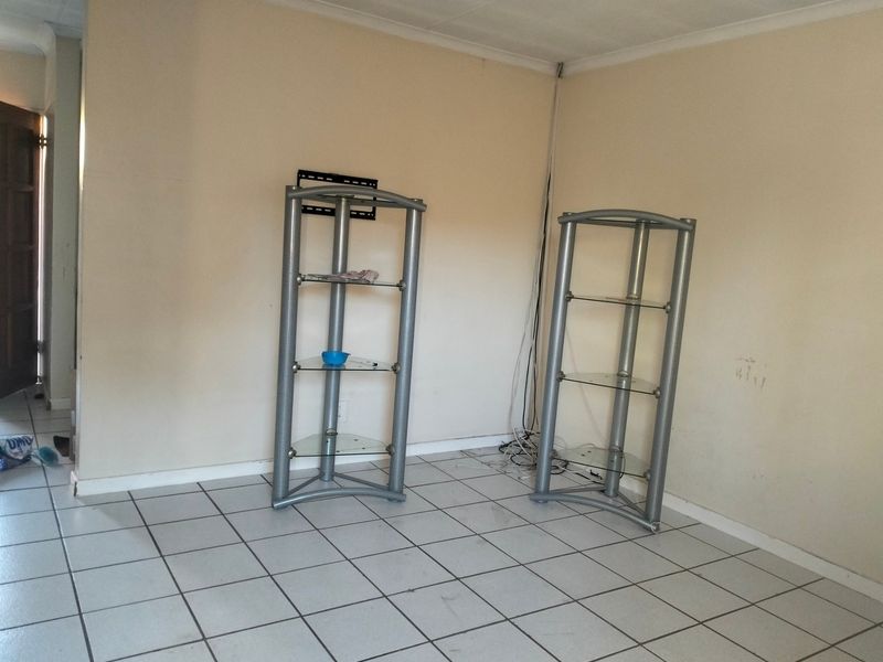 An empty living room area featuring tiled flooring and a wall-mounted television bracket, requiring minor cosmetic updates to the walls and wiring management.