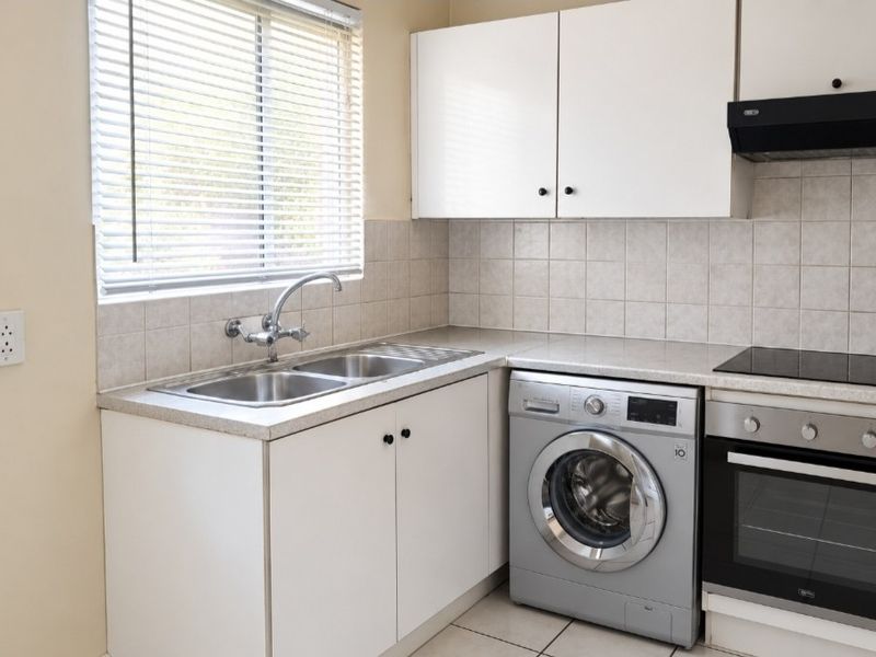 A functional kitchen featuring white cabinetry, tiled backsplash, laminate countertops, a double sink, and integrated oven with hob and extractor fan.