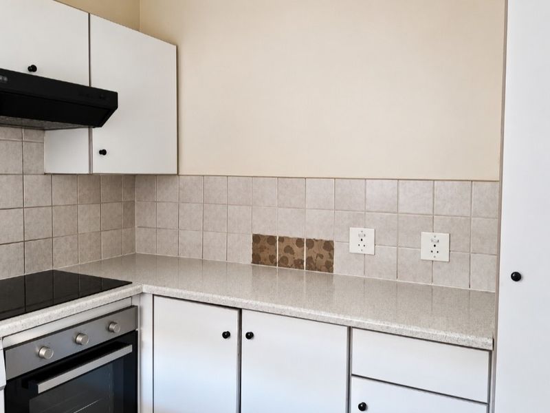 A functional kitchen area featuring built-in cabinetry, a hob, an oven, and a tiled backsplash with neutral countertops.