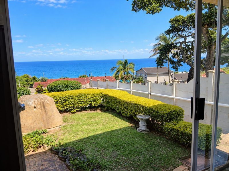 A scenic view of the ocean from a private garden area, featuring a well-maintained hedge and secure boundary wall.
