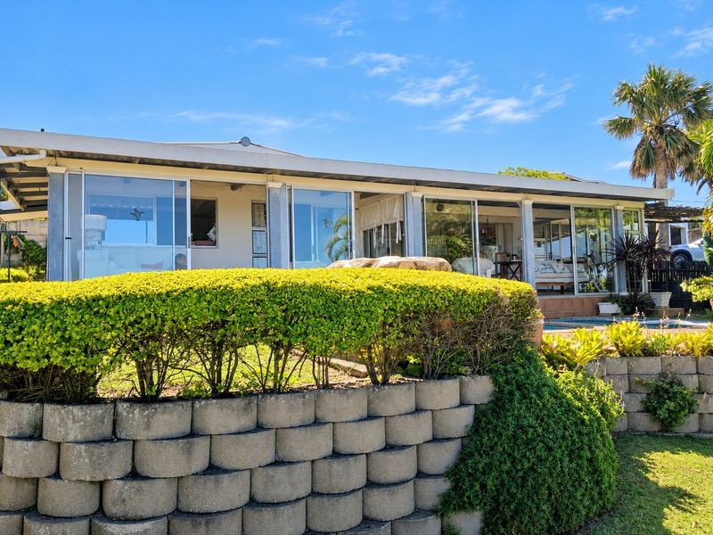 Rear view of the property featuring a tiered retaining wall, landscaped garden, covered patio with large sliding glass doors, and a swimming pool.