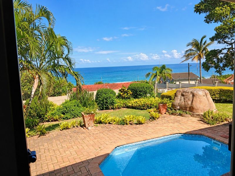 A well-maintained outdoor pool area featuring brick paving, landscaped garden, and a scenic ocean view.