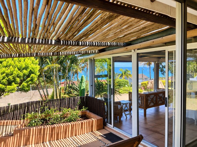 Covered patio area featuring a rustic timber pole pergola, tiled flooring, and sliding glass doors leading to a garden with ocean views.