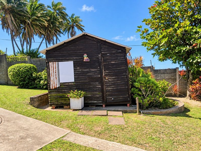 A weathered timber utility shed located in the garden, featuring a corrugated metal panel and set on a concrete base.