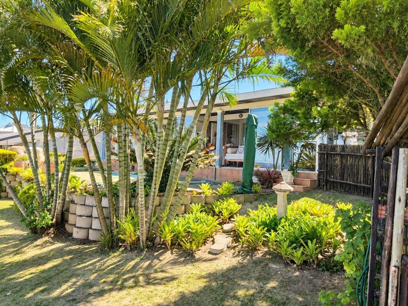 A view of the rear exterior featuring a landscaped garden with a retaining wall, mature palms, and a tiled patio area with sliding glass doors.